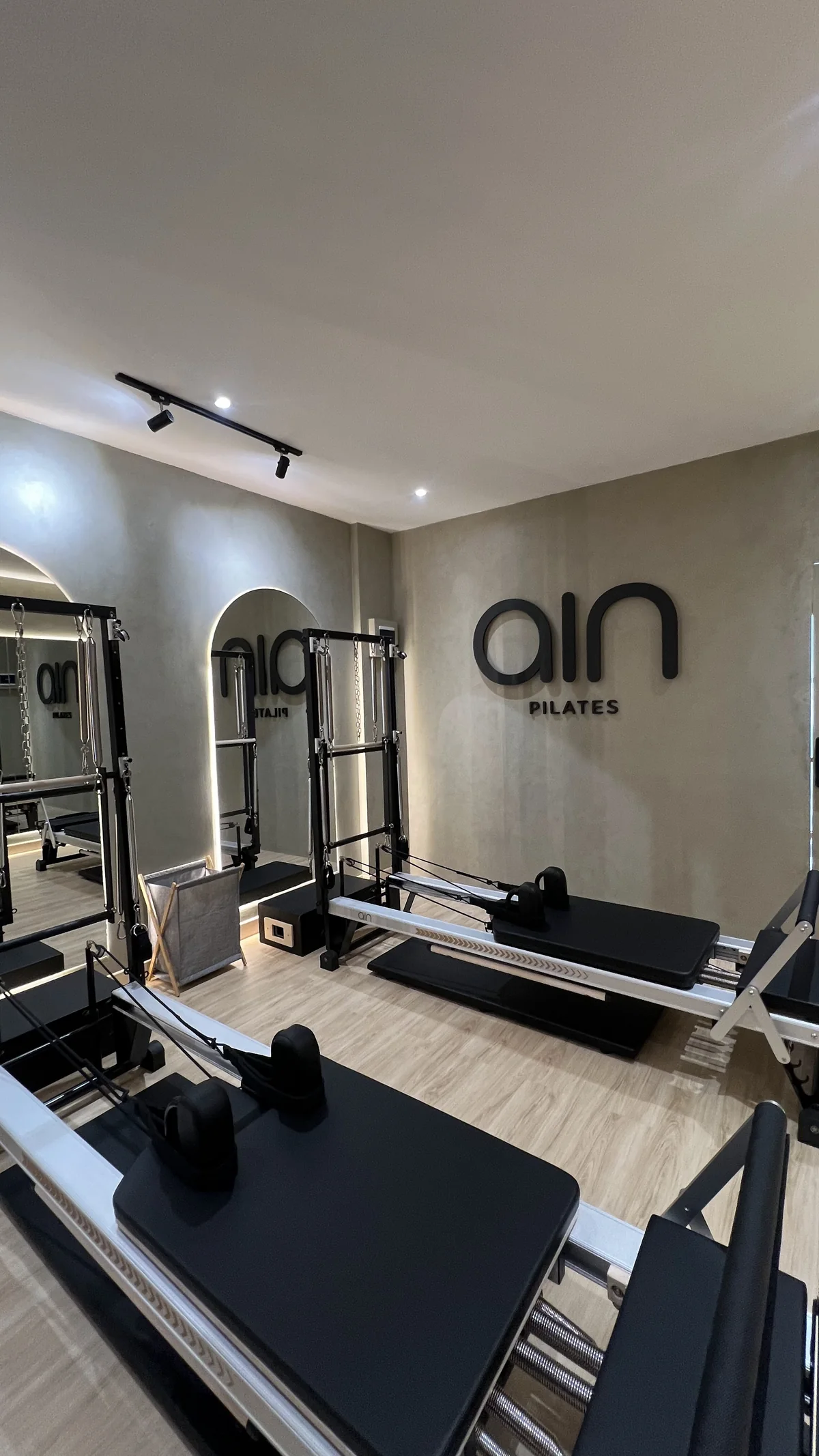 Ain's reformer room: black reformers, a tower by the arched mirror, the ain wordmark on a warm grey wall