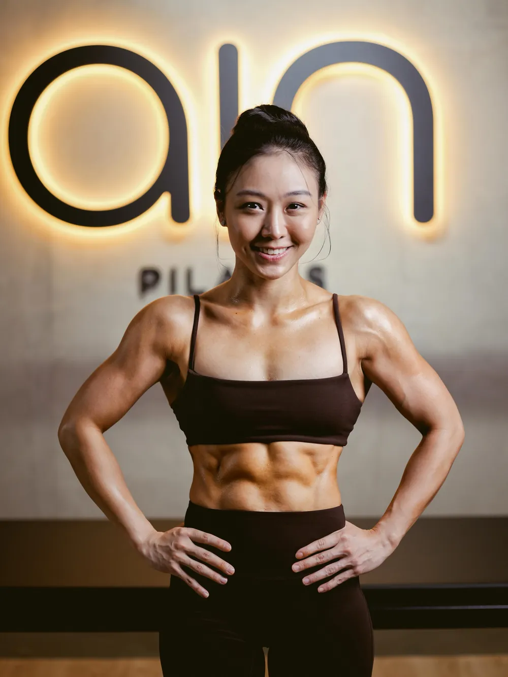 Ocha, Ain's founder, hands on hips in front of the lit wordmark